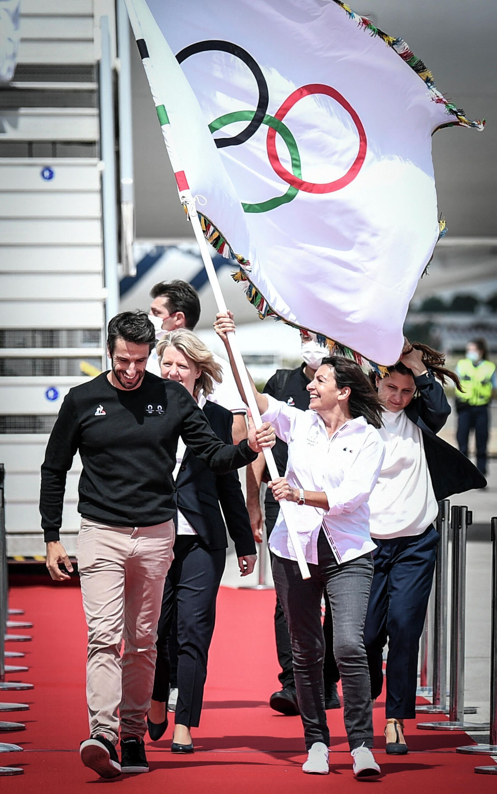 President of the Paris Organising Committee of the 2024 Olympic and Paralympic Games Tony Estanguet (front L) and Paris mayor Anne Hidalgo (front R) carry the Olympic flag from the plane, marking the handover from Japan to the next Games in Paris 2024, as French athletes return from the Tokyo Olympic 2020 games at Roissy-Charles de Gaulle airport, north of Paris on August 9, 2021. - Sputnik International, 1920, 12.09.2021