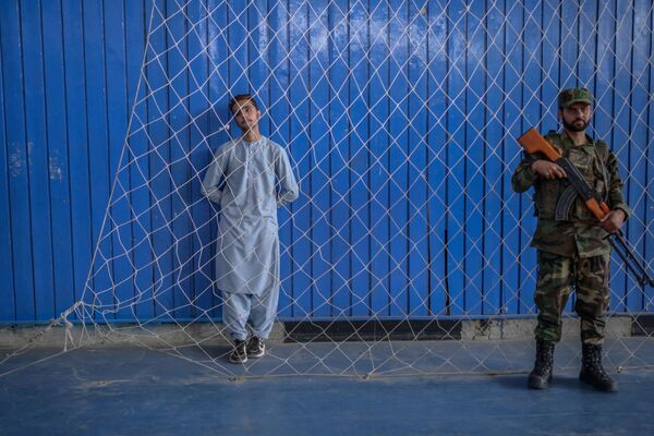 A young athlete (L) stands next to a Taliban fighter as others perform their skills during an event organised for the visit of the Taliban&#x27;s director of physical education and sports, Bashir Ahmad Rustamzai (not pictured), at a gymnasium in Kabul on 14 September 2021. - Sputnik International