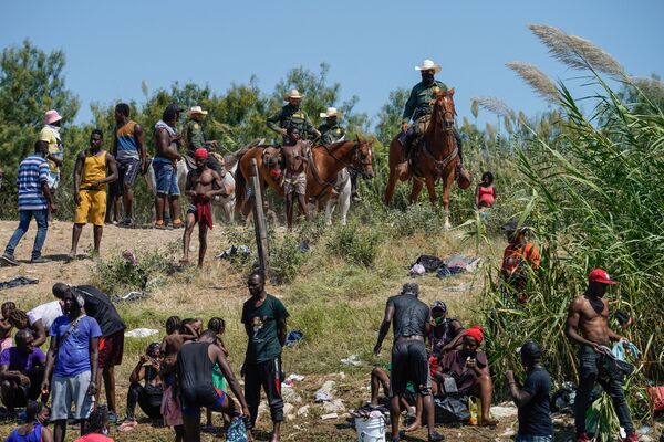 Mounted United States Border Patrol agents look on as Haitian migrants sit on the river bank near an encampment on the banks of the Rio Grande near the Acuna Del Rio International Bridge in Del Rio, Texas on 19 September 2021.  - Sputnik International