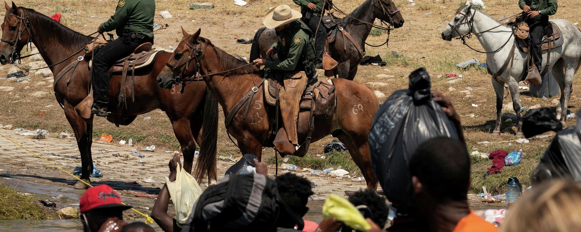 Migrants seeking asylum in the U.S. cross the Rio Grande river into the U.S. after obtaining food and supplies in Mexico as the U.S. Border Patrol agents monitor on a horse on the U.S. side of the bank near the International Bridge between Mexico and the U.S., in Del Rio Texas, U.S., where they wait to be processed, as seen from Ciudad Acuna, Mexico, September 20, 2021. - Sputnik International, 1920, 21.09.2021