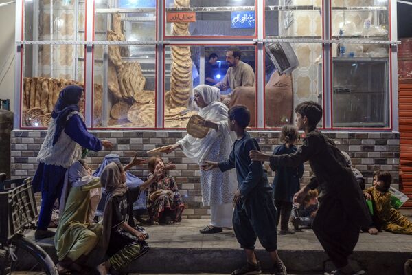 A woman gives bread to hungry young people in front of a bakery in Kabul on 19 September  2021. - Sputnik International