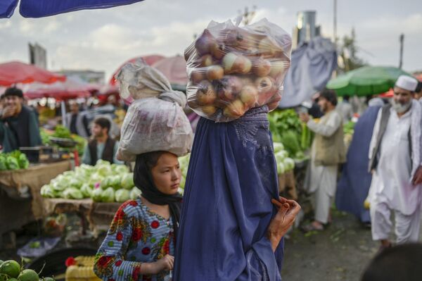 In this picture taken on 22 September 2021, a burqa-clad woman carries a bag of onions on her head at a market in Kabul. - Sputnik International