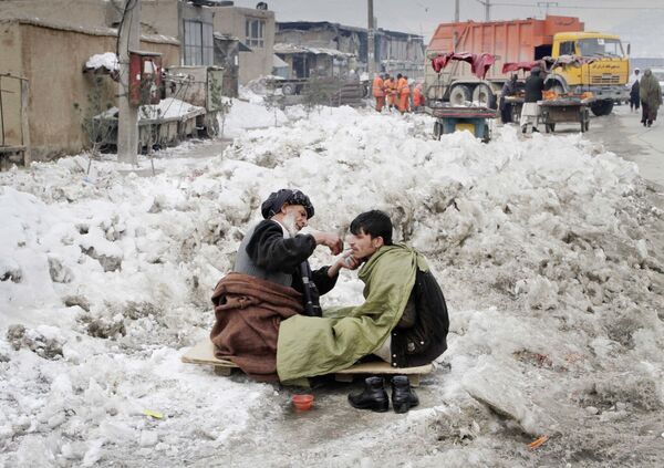 An Afghan street barber sits on a plank in the snow as he trims the moustache of a customer in Kabul, 9 February 2012.  - Sputnik International