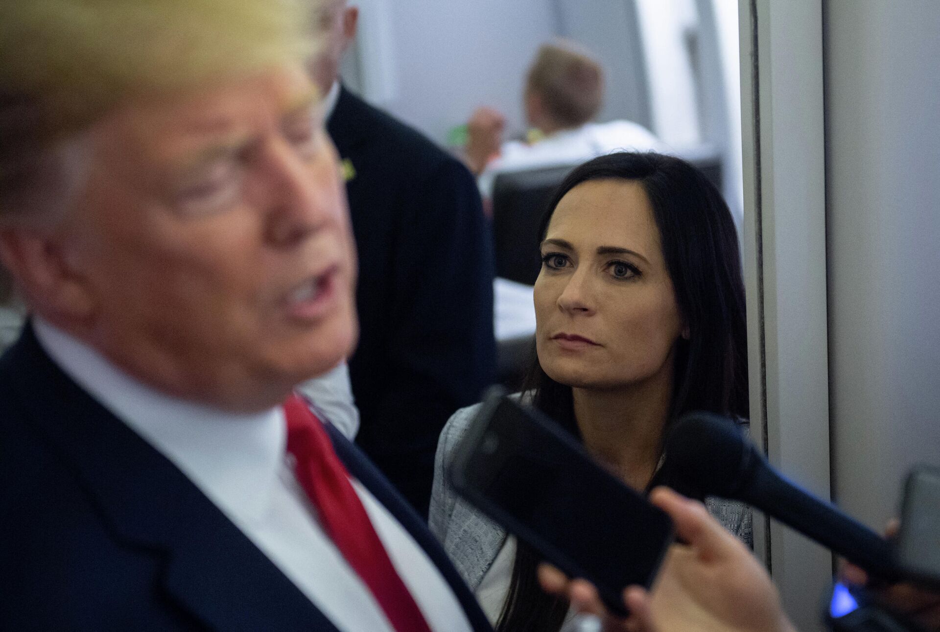 In this file photo former White House Press Secretary Stephanie Grisham listens as US President Donald Trump speaks to the media aboard Air Force One while flying between El Paso, Texas and Joint Base Andrews in Maryland, August 7, 2019. - An aide dubbed the Music Man was tasked with playing calming tunes for Donald Trump when he went into rages, according to a scandal-filled book by a former press secretary.Stephanie Grisham, notorious for not giving a single televised press conference while serving as Trump's chief spokeswoman, writes in I'll Take Your Questions Now that her boss went into terrifying rants.The former president and his wife Melania have vociferously condemned the book, excerpts of which appeared on September 28, 2021 in The New York Times and Washington Post. - Sputnik International, 1920, 06.10.2021