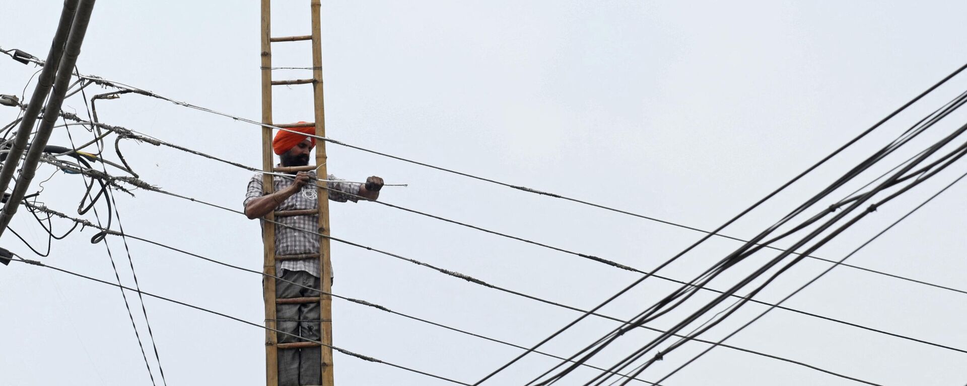 An employee of the Indian Punjab State Power Corporation Ltd, works on overhead electric cables in Amritsar on July 10, 2021 - Sputnik International, 1920, 11.10.2021