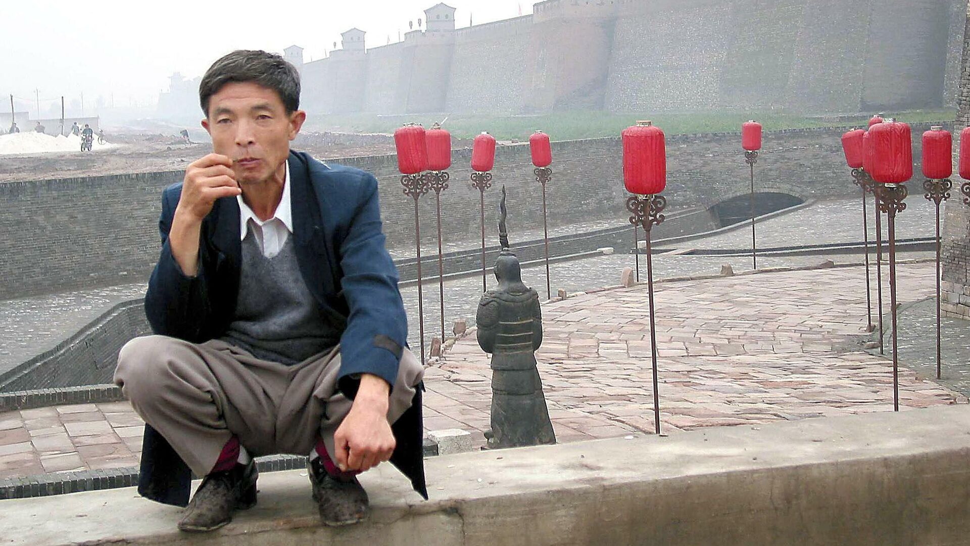 A man sits near a gate to the ancient city of Pingyao, in northern China, 21 September, 2002, which is now one of China's top tourist destinations - Sputnik International, 1920, 12.10.2021