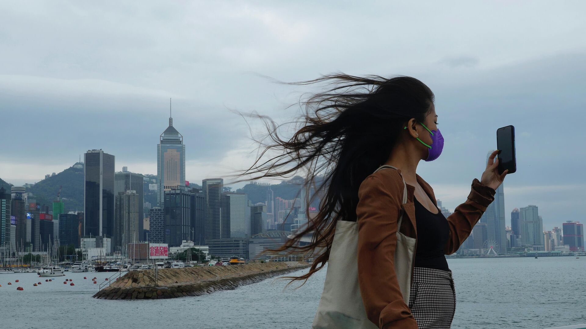 A woman poses for a selfie at the waterfront of Victoria Habour in strong winds while a typhoon approaches Hong Kong Tuesday, Oct. 12, 2021. The Hong Kong Observatory said it will consider issuing the number 8 signal between 4pm and 6pm on Tuesday as Severe Tropical Storm Kompasu edges closer to the city. - Sputnik International, 1920, 13.10.2021