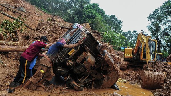 Rescue workers push a overturned vehicle stuck in the mud and debris at a site of a landslide claimed to be caused by heavy rains in Kokkayar in India's Kerala state on October 17, 2021 - Sputnik International