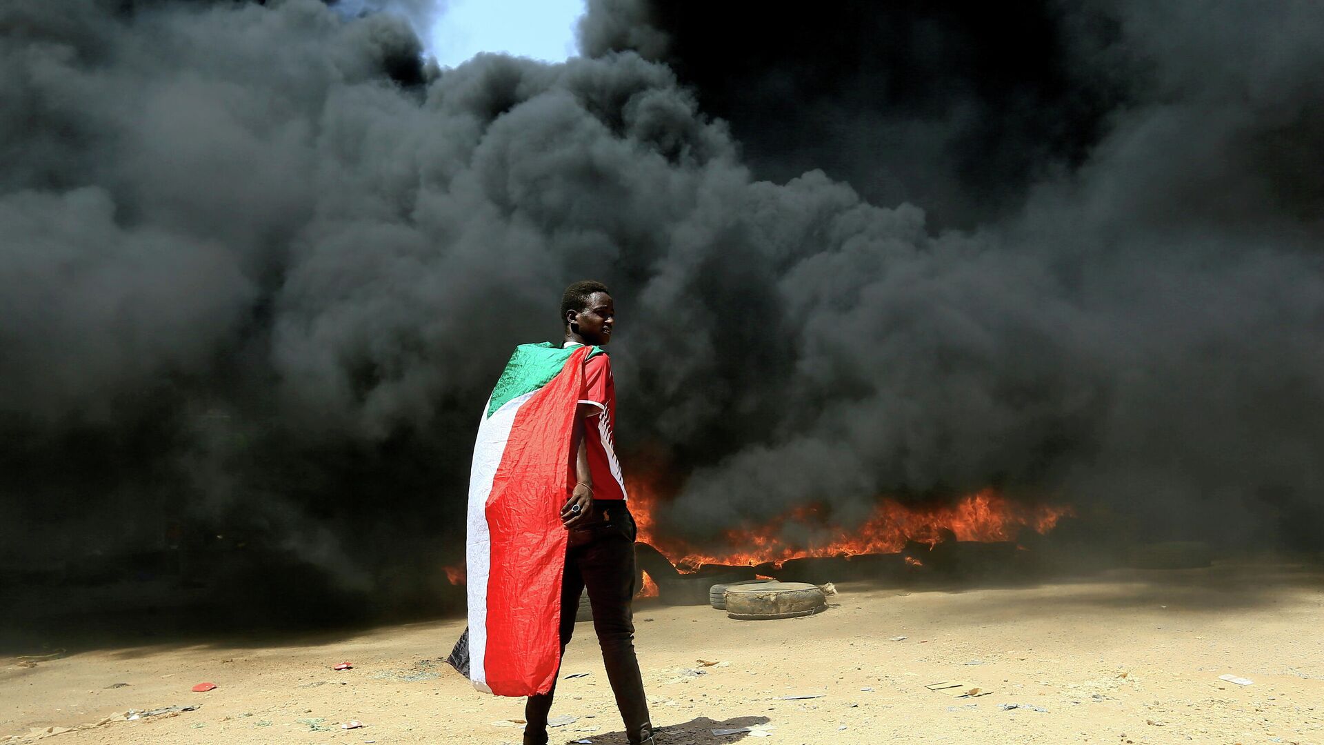 A person wearing a Sudan's flag stand in front of a burning pile of tyres during a protest  against prospect of military rule in Khartoum, Sudan October 21, 2021 - Sputnik International, 1920, 27.10.2021