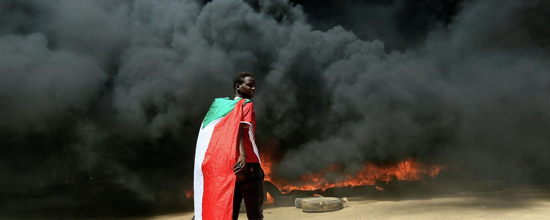 A person wearing a Sudan's flag stand in front of a burning pile of tyres during a protest  against prospect of military rule in Khartoum, Sudan October 21, 2021 - Sputnik International, 1920, 25.10.2021