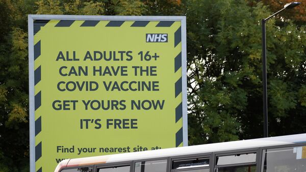People on a bus pass a sign encouraging the public to get their COVID-19 vaccine doses in Manchester - Sputnik International