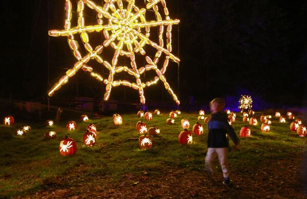 A kid walks by a giant spiderweb made of illuminated carved pumpkins during &quot;The Great Jack O&#x27;Lantern Blaze&quot; at Van Cortlandt Manor on 27 October 2021 in Croton-on-Hudson, New York, ahead of Halloween. - Sputnik International