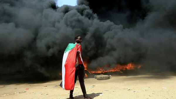 A person wearing a Sudan's flag stand in front of a burning pile of tyres during a protest  against prospect of military rule in Khartoum, Sudan October 21, 2021. - Sputnik International