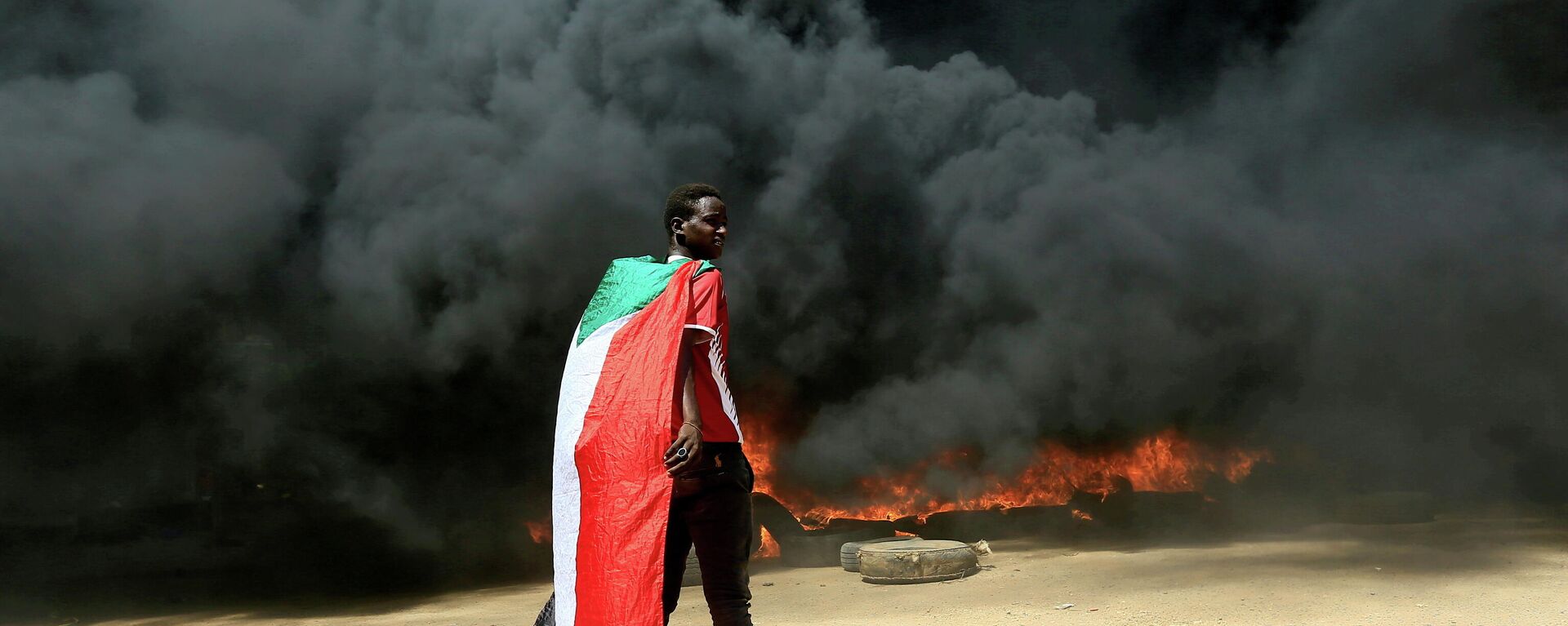 A person wearing a Sudan's flag stand in front of a burning pile of tyres during a protest  against prospect of military rule in Khartoum, Sudan October 21, 2021. - Sputnik International, 1920, 24.11.2021
