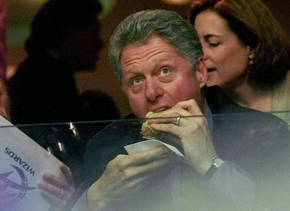 President Clinton eats a sandwich near the beginning of a sporting event as he eyes the scoreboard from behind a panel of plexiglass  at the new MCI Center in Washington, DC on Tuesday 2 December 1997. - Sputnik International