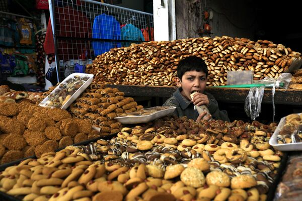 A boy eats a sandwich while surrounded by pastries at the open air market in Manbij in Syria on 28 March 2018. - Sputnik International