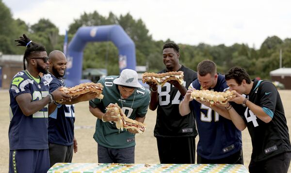 A wall of NFL players - from left, Seattle Seahawks&#x27; cornerback Neiko Thorpe, Tennessee Titans&#x27; defensive end Jurrell Casey, Philadelphia Eagles&#x27; wide receiver Mack Hollins, Oakland Raiders&#x27; tight end Jared Cook, Los Angeles Chargers&#x27; linebacker Kyle Emanuel and Jacksonville Jaguars&#x27; kicker Josh Lambo - pose with large sandwiches during an NFL flag schools event at King&#x27;s House Sports Ground in Chiswick, west London on Wednesday 18 July 2018. - Sputnik International