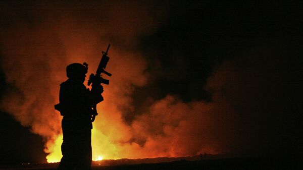 Sgt. Robert B. Brown from Fayetteville, N.C. with Regimental Combat Team 6, Combat Camera Unit watches over the civilian Fire Fighters at the burn pit as smoke and flames rise into the night sky behind him on May 25th, 2007. - Sputnik International