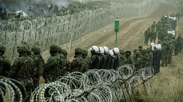 Polish soldiers and police watch migrants at the Poland/Belarus border near Kuznica, Poland, in this photograph released by the Territorial Defence Forces, November 12, 2021 - Sputnik International