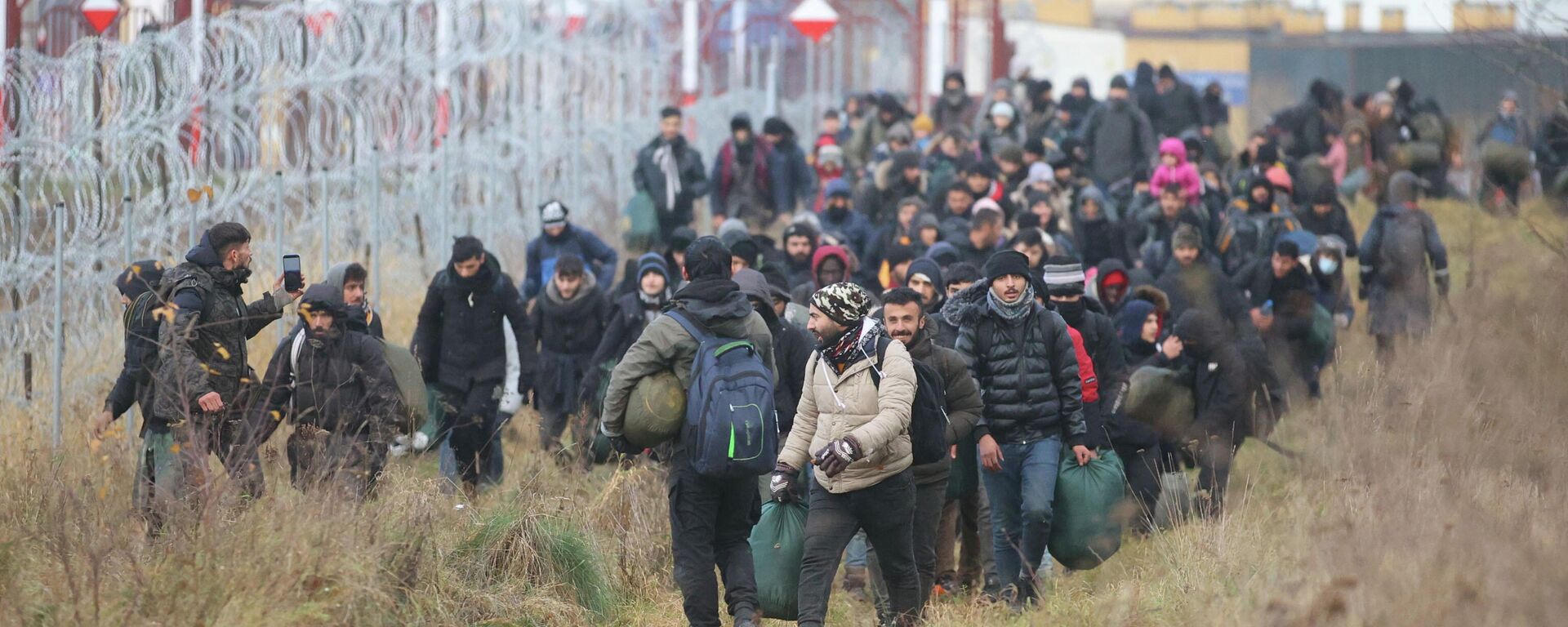 A group of migrants walk near a barbed wire fence while moving toward a makeshift camp on the Belarusian-Polish border in the Grodno region, Belarus November 12, 2021. Leonid Scheglov/BelTA/Handout via REUTERS  ATTENTION EDITORS - THIS IMAGE HAS BEEN SUPPLIED BY A THIRD PARTY. NO RESALES. NO ARCHIVE. MANDATORY CREDIT. - Sputnik International, 1920, 18.11.2021