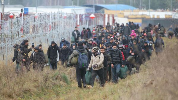 A group of migrants walk near a barbed wire fence while moving toward a makeshift camp on the Belarusian-Polish border in the Grodno region, Belarus November 12, 2021. Leonid Scheglov/BelTA/Handout via REUTERS  ATTENTION EDITORS - THIS IMAGE HAS BEEN SUPPLIED BY A THIRD PARTY. NO RESALES. NO ARCHIVE. MANDATORY CREDIT. - Sputnik International