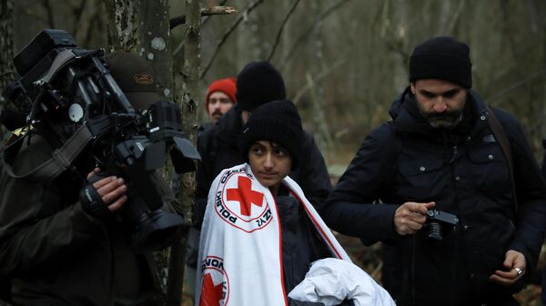 A migrant wrapped in a blanket of Red Cross is surrounded by journalists in a forest near the Polish-Belarusian border outside Narewka, Poland November 9, 2021 - Sputnik International
