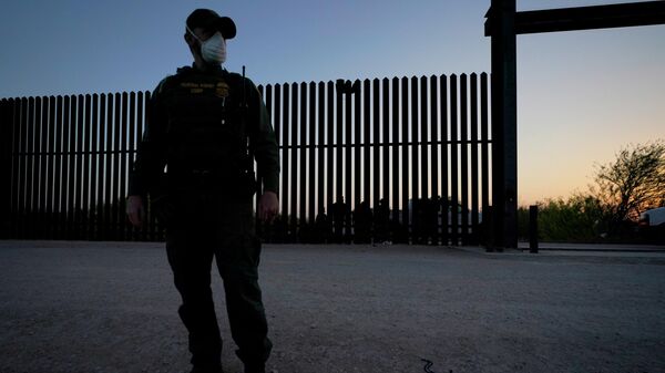 In this March 21, 2021 file photo, a U.S. Customs and Border Protection agent looks on near a gate on the U.S.-Mexico border wall as agents take migrants into custody, in Abram-Perezville, Texas. - Sputnik International
