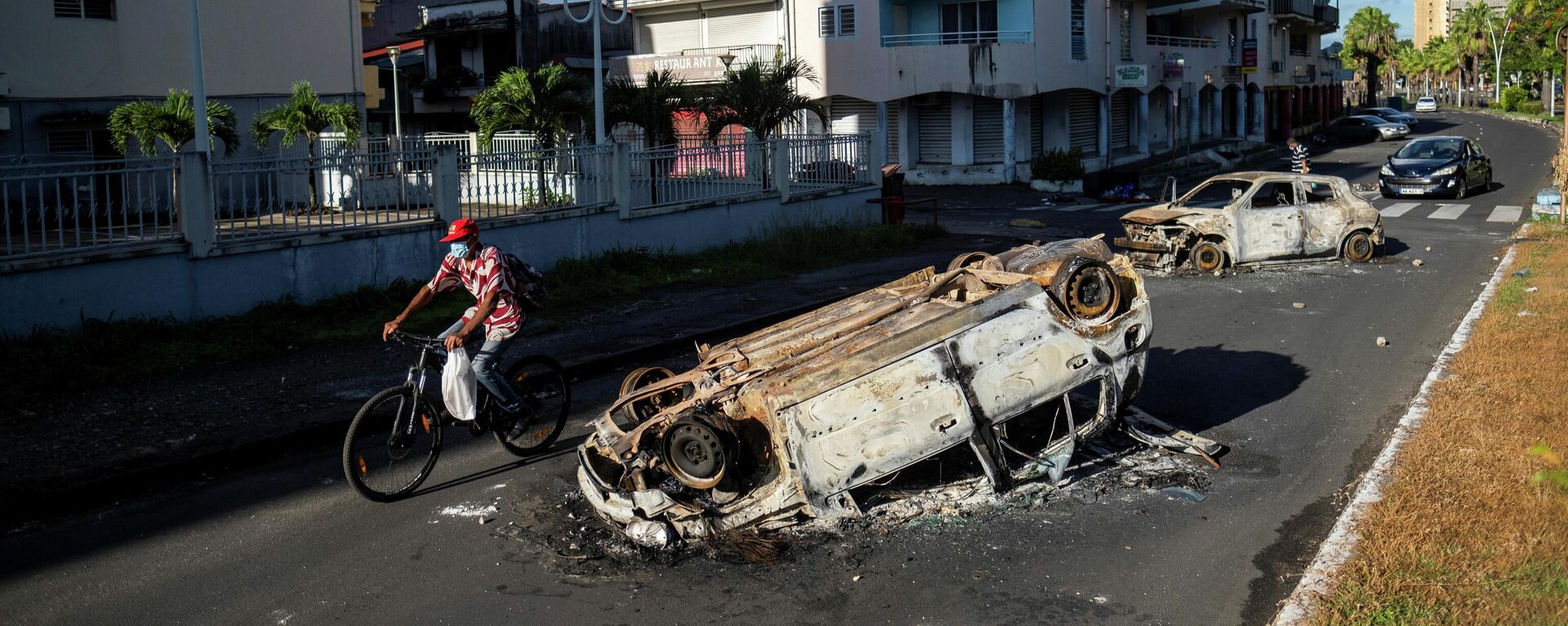 A man rides his bicycle past burned cars after violent demonstrations which broke out over coronavirus disease (COVID-19) protocols, in Pointe-a-Pitre, Guadeloupe November 21, 2021 - Sputnik International, 1920, 23.11.2021