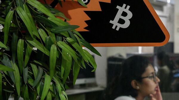 In this picture taken on November 23, 2021 an employee works on her workstation on the backdrop of the cryptocurrency symbol of Bitcoin pasted on a glass door of a private office in Bangalore - Sputnik International