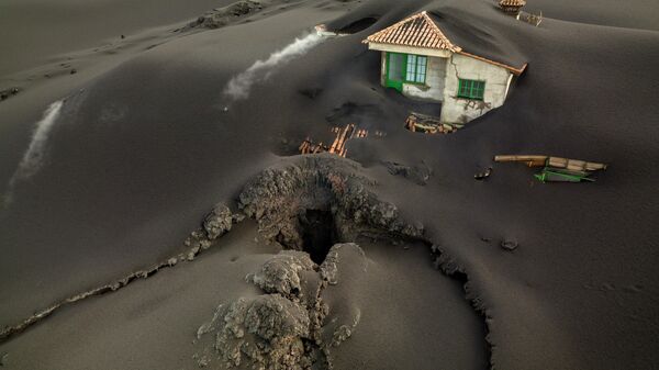 FILE - A fissure is seen next to a house covered with ash on the Canary island of La Palma, Spain, Dec. 1 2021. Authorities on a Spanish island are declaring a volcanic eruption that has caused widespread damage but no casualties officially finished, following ten days of no significant sulfur dioxide emissions, lava flows or seismic activity. But the emergency in La Palma, the northwesternmost of the Atlantic Ocean's Canary Islands, is not over yet, said the director of the archipelago’s volcanic emergency committee, or Pevolca, Julio Pérez. - Sputnik International