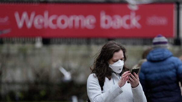 A woman wearing a mask to protect against the coronavirus looks at her phone in Trafalgar Square, in London - Sputnik International