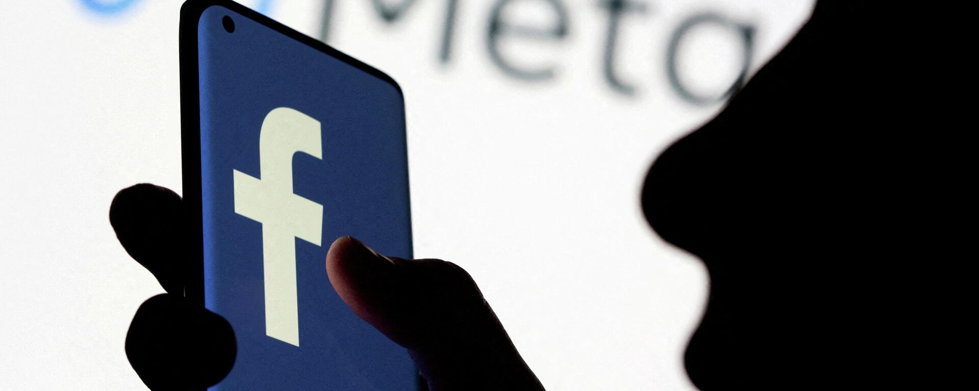 A woman holds smartphone with Facebook logo in front of a displayed Facebook's new rebrand logo Meta in this illustration picture taken October 28, 2021 - Sputnik International, 1920, 03.02.2022