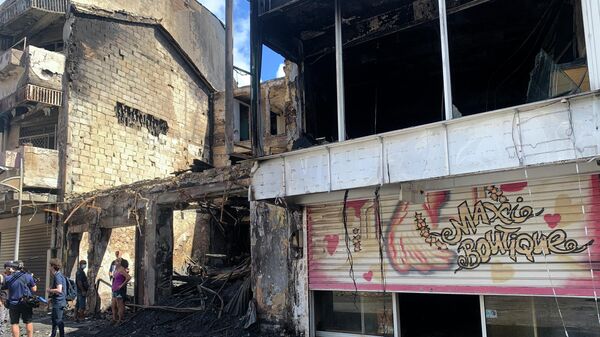 Reporters work by charred shop and building in a s street of Pointe-a-Pitre, Guadeloupe island, Sunday, Nov.21, 2021. French authorities are sending police special forces to the Caribbean island of Guadeloupe, an overseas territory of France, as protests over COVID-19 restrictions erupted into rioting. In Pointe-a-Pitre, the island's largest urban area, clashes left three people injured, including a 80-year-old woman who was hit by a bullet while on her balcony. A firefighter and a police officer were also injured and several shops were looted there and in other towns. - Sputnik International