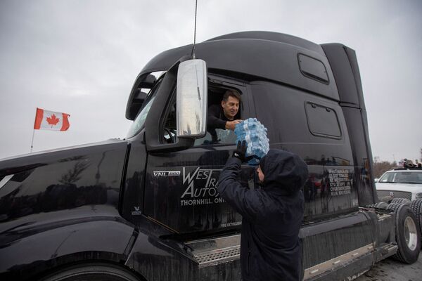 A supporter gives a case of bottled water to a driver gathering to support truck drivers on their way to Ottawa in protest against coronavirus vaccine mandates for cross-border truck drivers, in Toronto, Ontario, Canada, on 27 January 2022. - Sputnik International