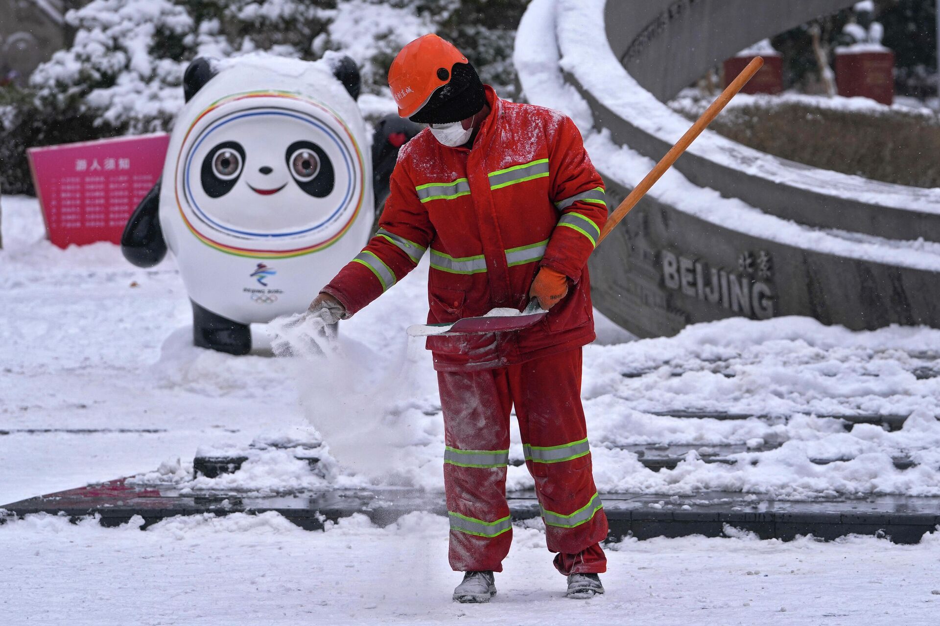 A worker sprays salt on the snow to prevent slipping near the Bing Dwen Dwen, the Beijing Winter Olympics mascot, on display at an Olympics monument during a snow fall in Beijing, Sunday, Feb. 13, 2022. - Sputnik International, 1920, 13.02.2022