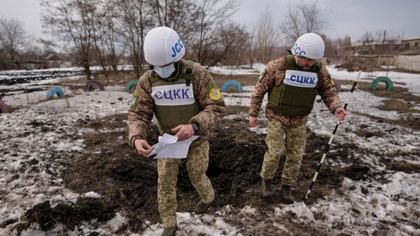 Members of the Joint Centre for Control and Coordination on ceasefire of the demarcation line, or JCCC, survey a crater from an artillery shell that landed near a school in Vrubivka, in the Lugansk region, eastern Ukraine, Thursday, Feb. 17, 2022.  - Sputnik International