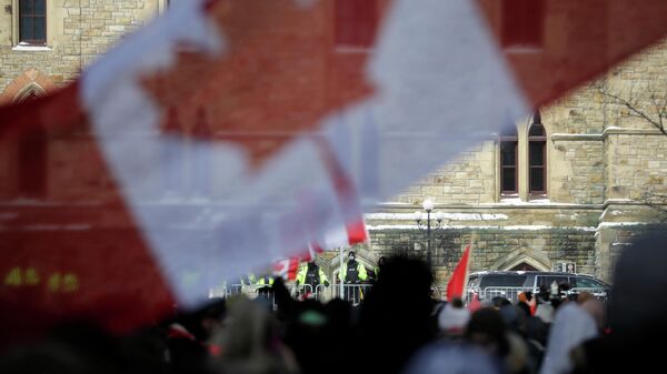 Canadian police officers watch while demonstrators hold Canadian flags, as they work to restore normality to the capital while trucks and demonstrators continue to occupy the downtown core for more than three weeks to protest against pandemic restrictions in Ottawa, Ontario, Canada, February 19, 2022.  REUTERS/Carlos Osorio - Sputnik International