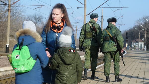 Armed people patrol the railway platform while residents wait for a train at the station in Makeevka to evacuate to Russia - Sputnik International