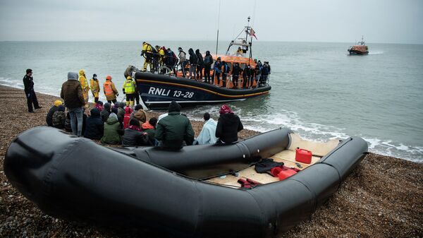 Migrants sit beside a boat used to cross the English Channel as more migrants are helped ashore from a RNLI (Royal National Lifeboat Institution) lifeboat at a beach in Dungeness, on the south-east coast of England, on November 24, 2021 - Sputnik International