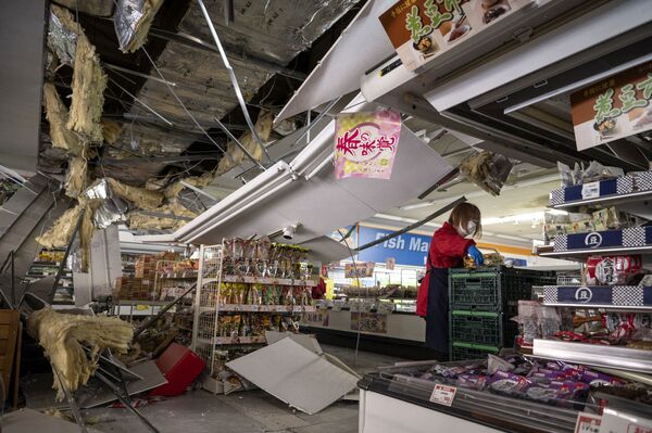 Сотрудник снимает товары с полок под поврежденным потолком в супермаркете в Сироиси, префектура Мияги - Sputnik International
