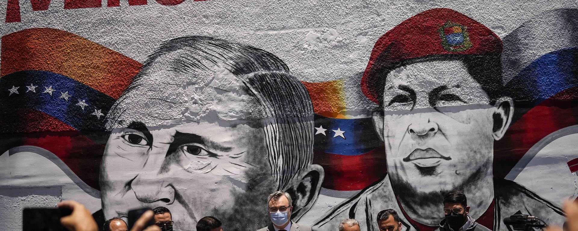 Russian Ambassador to Venezuela, Sergey Melik Bagdasarov, center, stands in front of a mural featuring Russian President Vladimir Putin and the late President Hugo Chavez, during an event to inaugurate a basketball and soccer venue, in the Catia neighborhood of Caracas, Venezuela, Saturday, April 2, 2022.  - Sputnik International, 1920, 17.08.2022