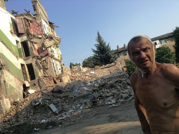 July 2014: 70-year-old Snezhnoe resident Viktor Stepanenko outside his apartment building, leveled by a Ukrainian missile. His wife and 11 others were killed in the attack. Stepanenko miraculously managed to survive after falling out of the fourth floor of the apartment bloc onto a spruce tree growing nearby. - Sputnik International
