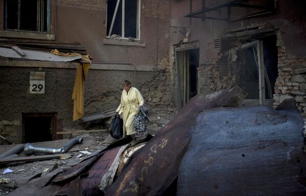 July 2014: A woman walks through the courtyard of a bombed out apartment building in Lugansk. - Sputnik International