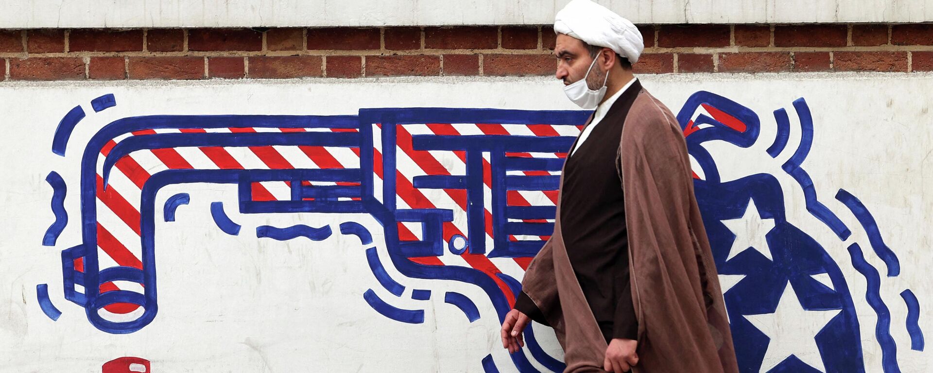 An Iranian cleric walks past an anti-US mural on a wall of the former United States embassy in the capital Tehran, on March 12, 2022. - Sputnik International, 1920, 10.04.2022