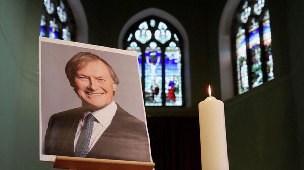 A candle and a portrait of British MP David Amess, who was stabbed to death during a meeting with constituents, are seen at the church of St Michael's and all Angels, in Leigh-on-Sea, Britain, October 17, 2021 - Sputnik International