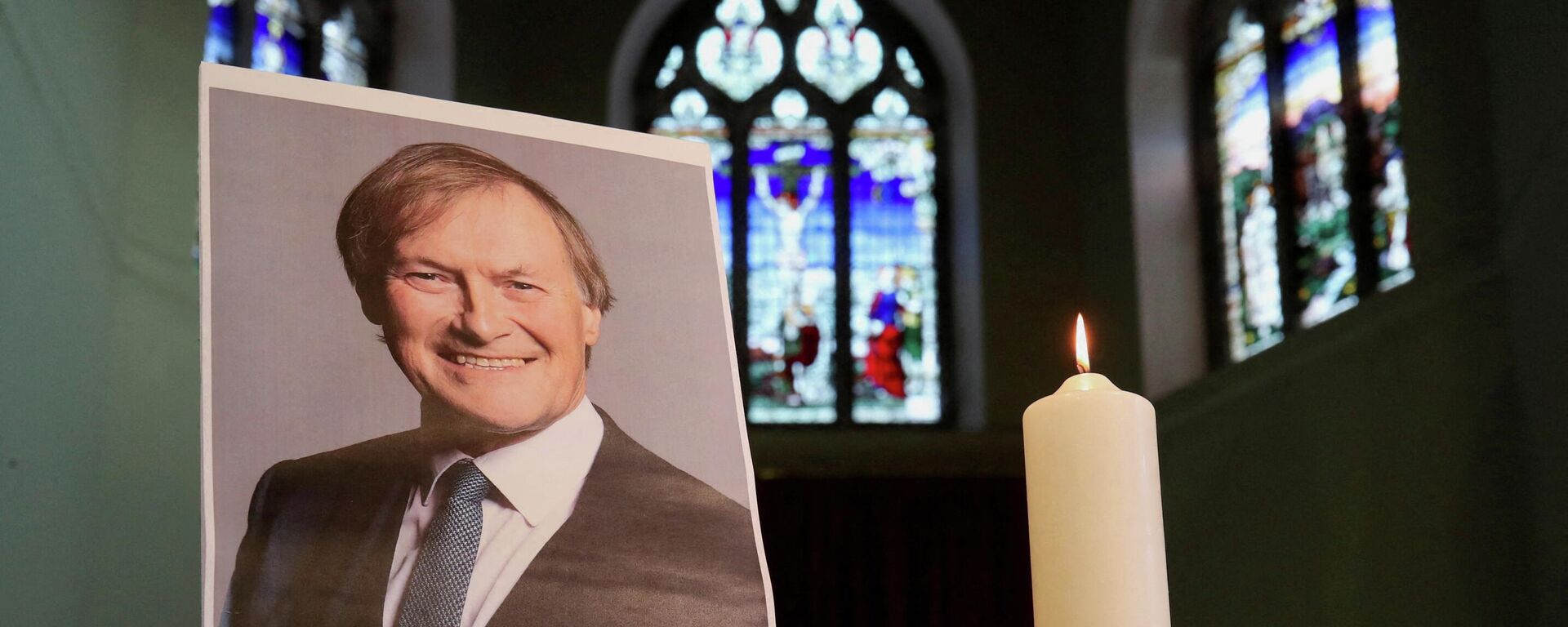 A candle and a portrait of British MP David Amess, who was stabbed to death during a meeting with constituents, are seen at the church of St Michael's and all Angels, in Leigh-on-Sea, Britain, October 17, 2021 - Sputnik International, 1920, 11.04.2022