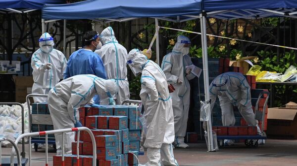 Workers wearing personal protective equipment (PPE) are seen next to food delivered by the local government for residents in a compound during a Covid-19 lockdown in the Jing'an district in Shanghai on April 10, 2022.  - Sputnik International