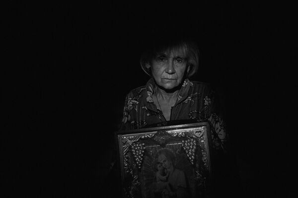 A woman holds up an icon of the Mother of God while waiting for Ukrainian forces to stop the shelling of the village of Vesyeloe in the Donetsk People’s Republic, 2015. Praying in the darkness in basements and waiting for shelling to stop – this is often all that the elderly, women and children can do. - Sputnik International