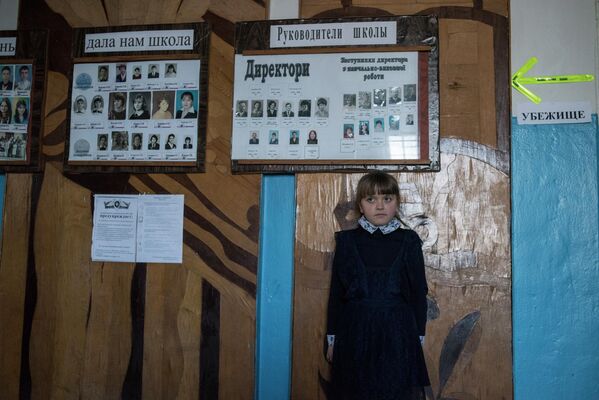 A girl in a school in the village of Sakhanka. Next to her are portraits of teachers and graduates. Signs marked “BOMB SHELTER”, accompanied by bright arrows, are plastered throughout the school. Children in Donbass schools have learned to distinguish the sound of incoming shells, and know well where the nearest bomb shelter is.  - Sputnik International