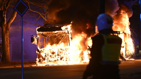 An anti-riot police officer stands next to a city bus burning in Malmo late April 16, 2022 - Sputnik International
